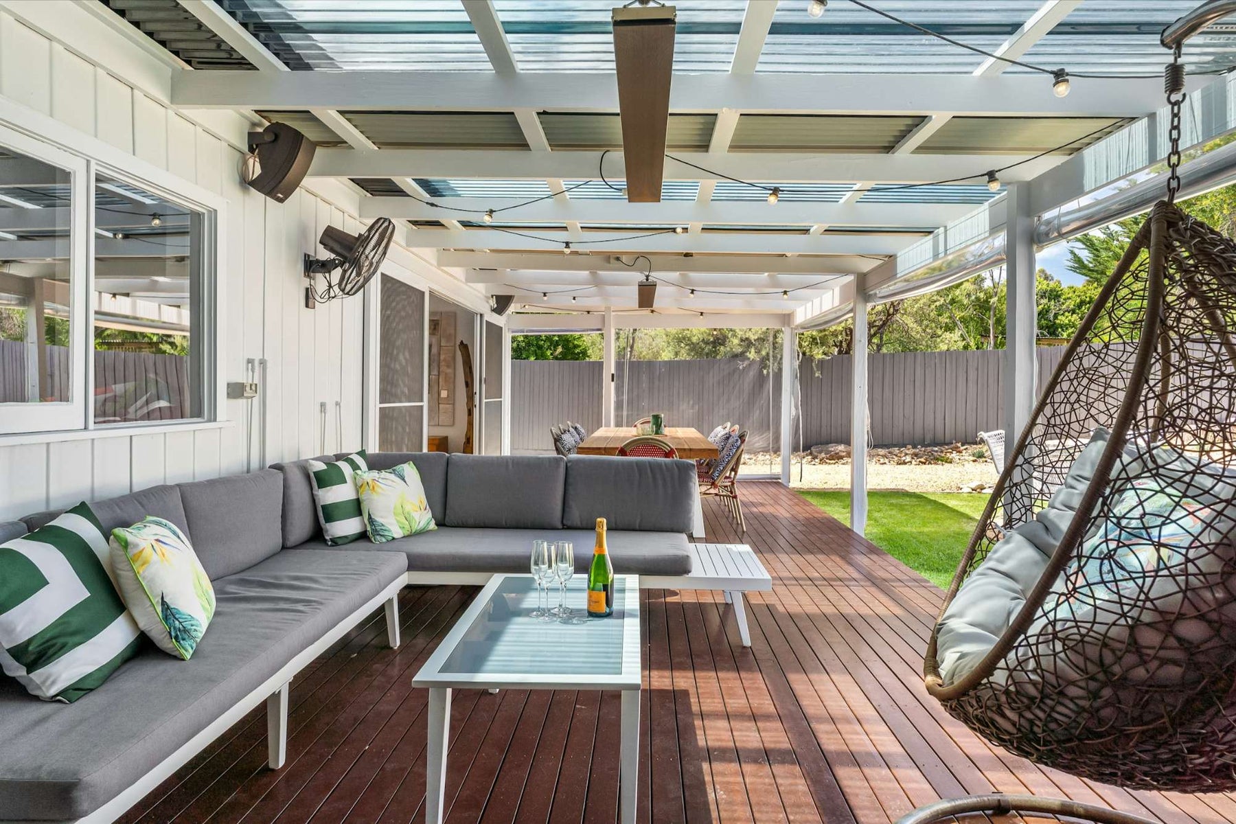The image shows a covered patio with a dining table and string lights, highlighting another of the 15 Ways to Make Your Backyard Summer-Ready by creating a versatile outdoor dining space