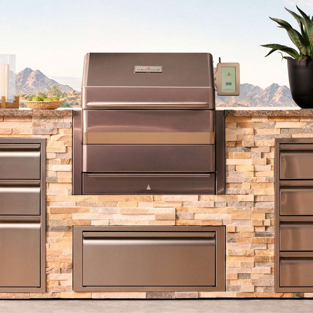 A Memphis Grills Pro Built-In ITC3 is beautifully installed in a stone-clad outdoor kitchen, set against a mountain backdrop