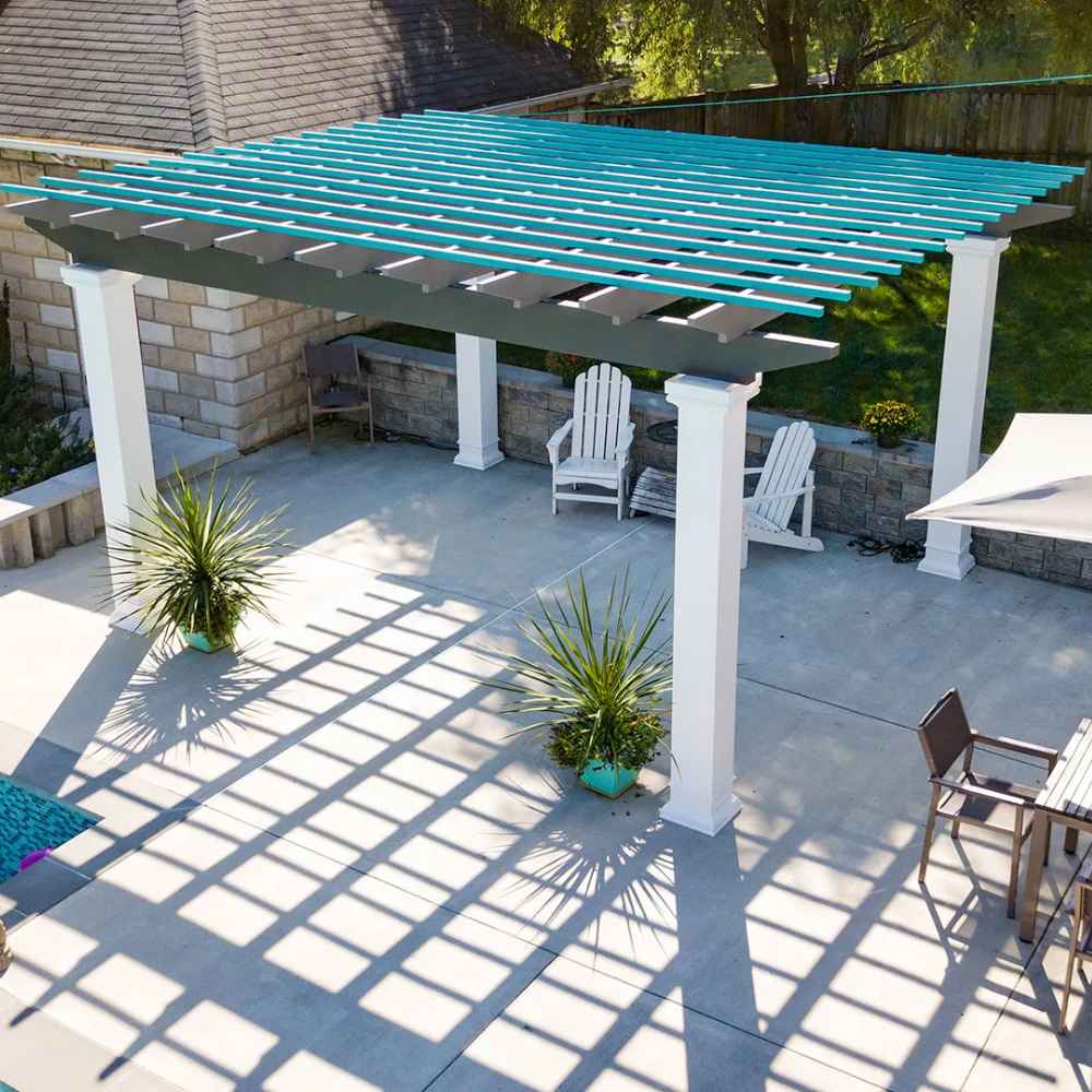 A concrete patio with lounge chairs is shaded by a bright blue and gray Structureworks Trex Pergola with white columns