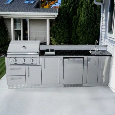 A backyard scene with the Sunstone Brazos 9ft Outdoor Grill & Cabinet Island Package installed on a patio near a house and lawn