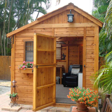 A cozy garden nook frames the Outdoor Living Today 8×12 Sunshed Garden Shed, its door open to reveal a furnished interior with a chair and small desk
