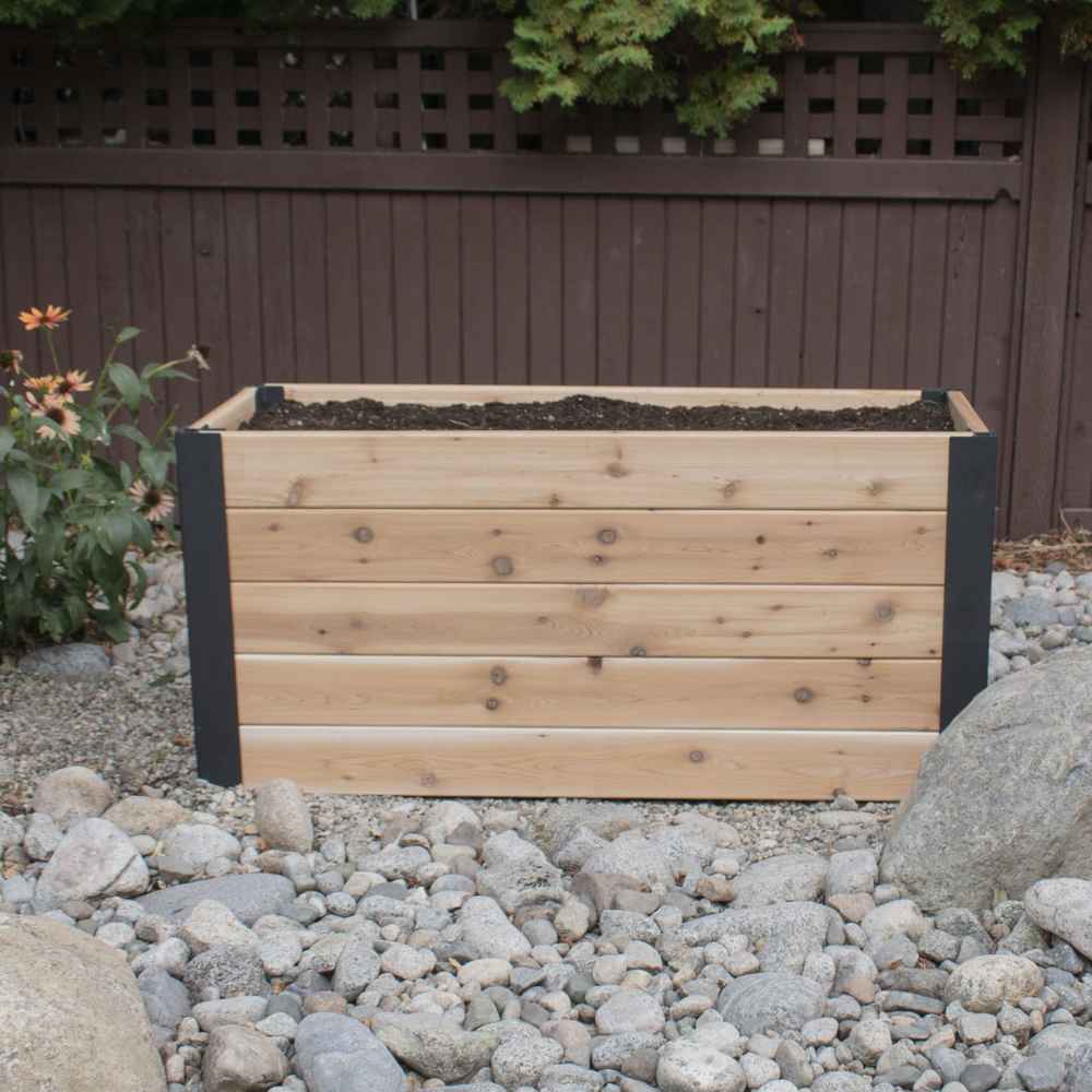 A front view shows the Outdoor Living Today 4×1.5 Urban Raised Garden Bed filled with fresh soil in a stone garden