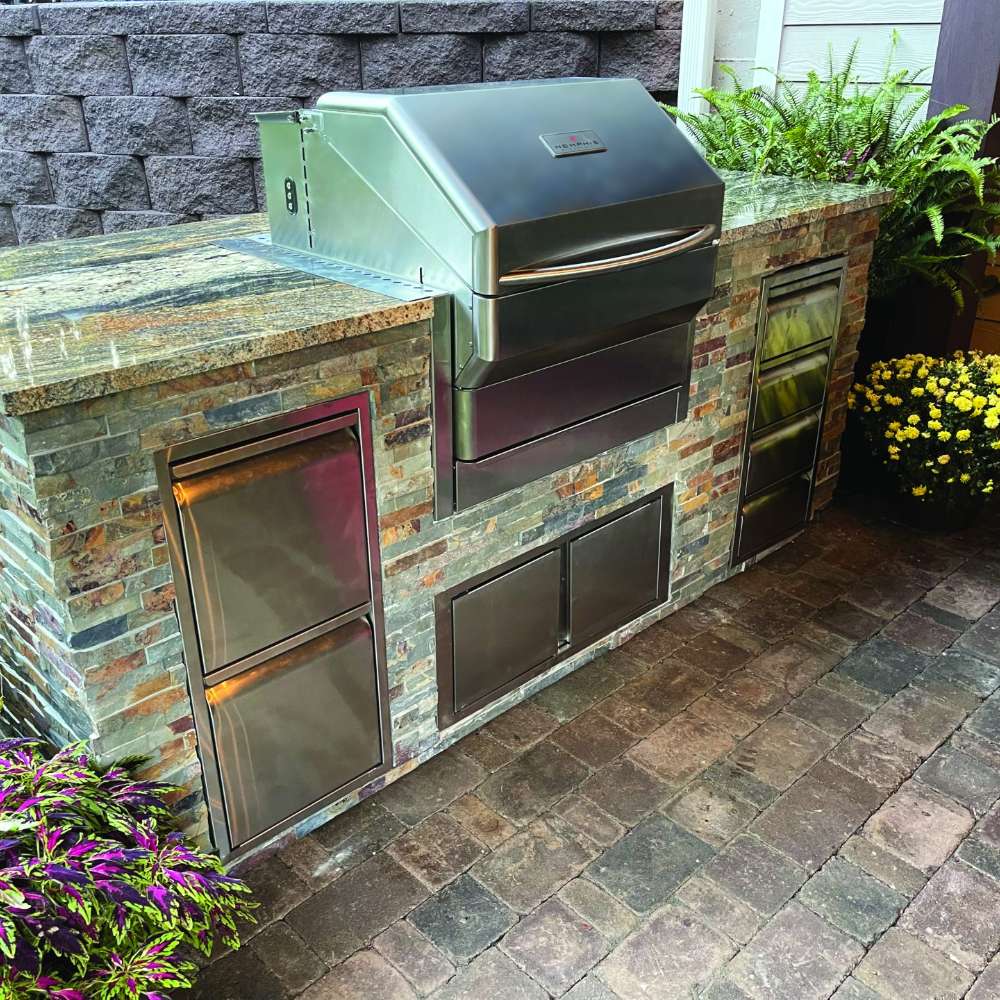 A sleek outdoor kitchen setup features a Memphis Grills Pro Built-In ITC3, seamlessly integrated into a stone island with stainless steel storage compartments
