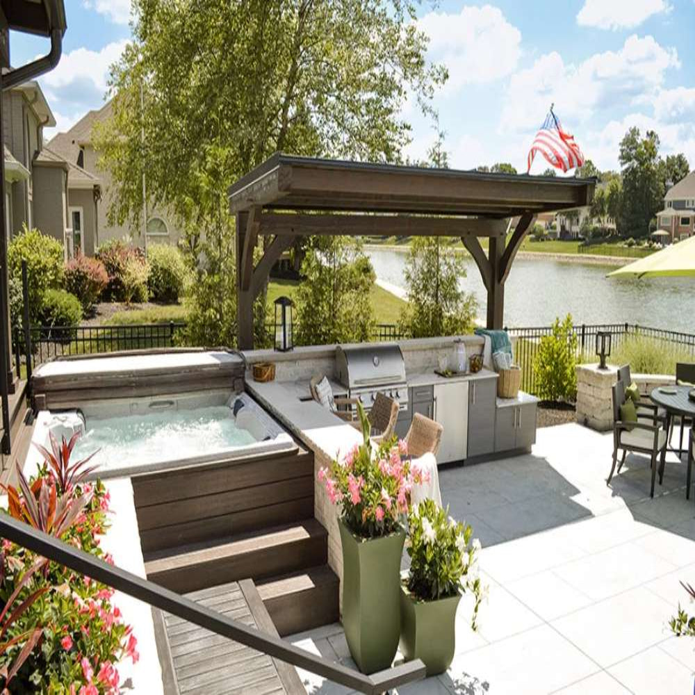 A spacious patio with a hot tub, grill, and bar seating is beautifully complemented by the Brookside Timber Frame Ledgefield Pavilion