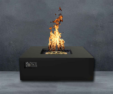 Black Warming Trends AON Steel Square Fire Pit Table is lit with bright flames against a dark gray wall background