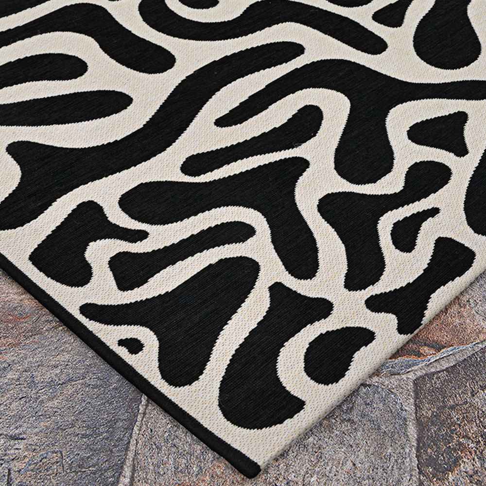 Close-up of the Couristan Castille Indoor/Outdoor Rug - Graffiti/Black-White shows the curved edge and flowing design on a textured stone floor