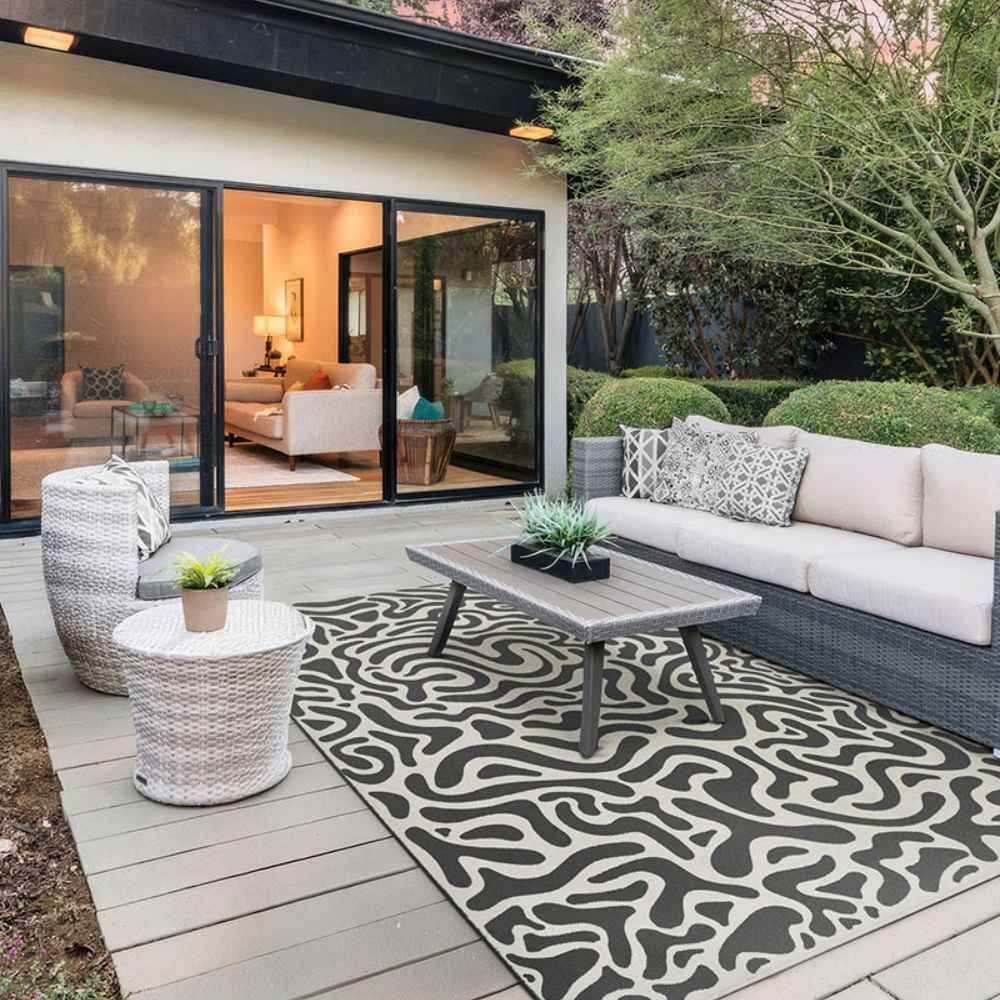 Couristan Castille Indoor/Outdoor Rug - Graffiti/Black-White decorates a modern outdoor patio, grounding a seating area with a wicker sofa and coffee table