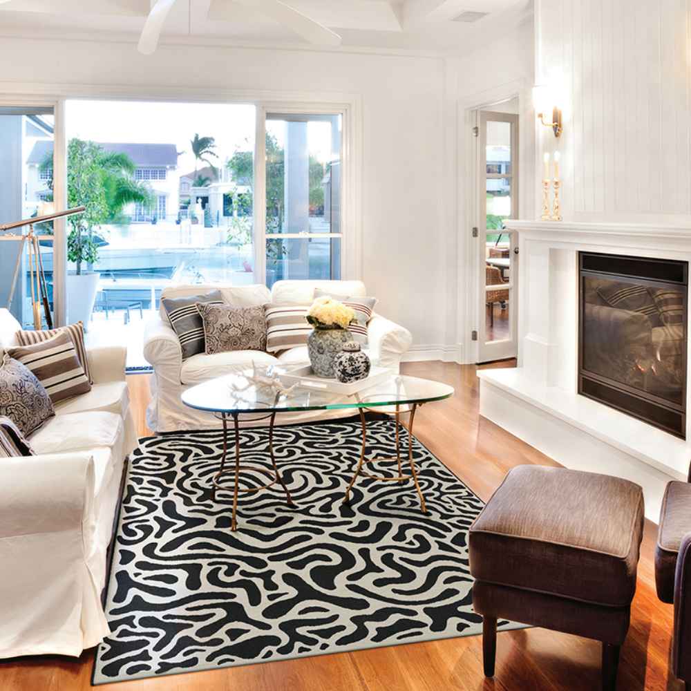 Couristan Castille Indoor/Outdoor Rug - Graffiti/Black-White is placed in a bright living room under a glass coffee table