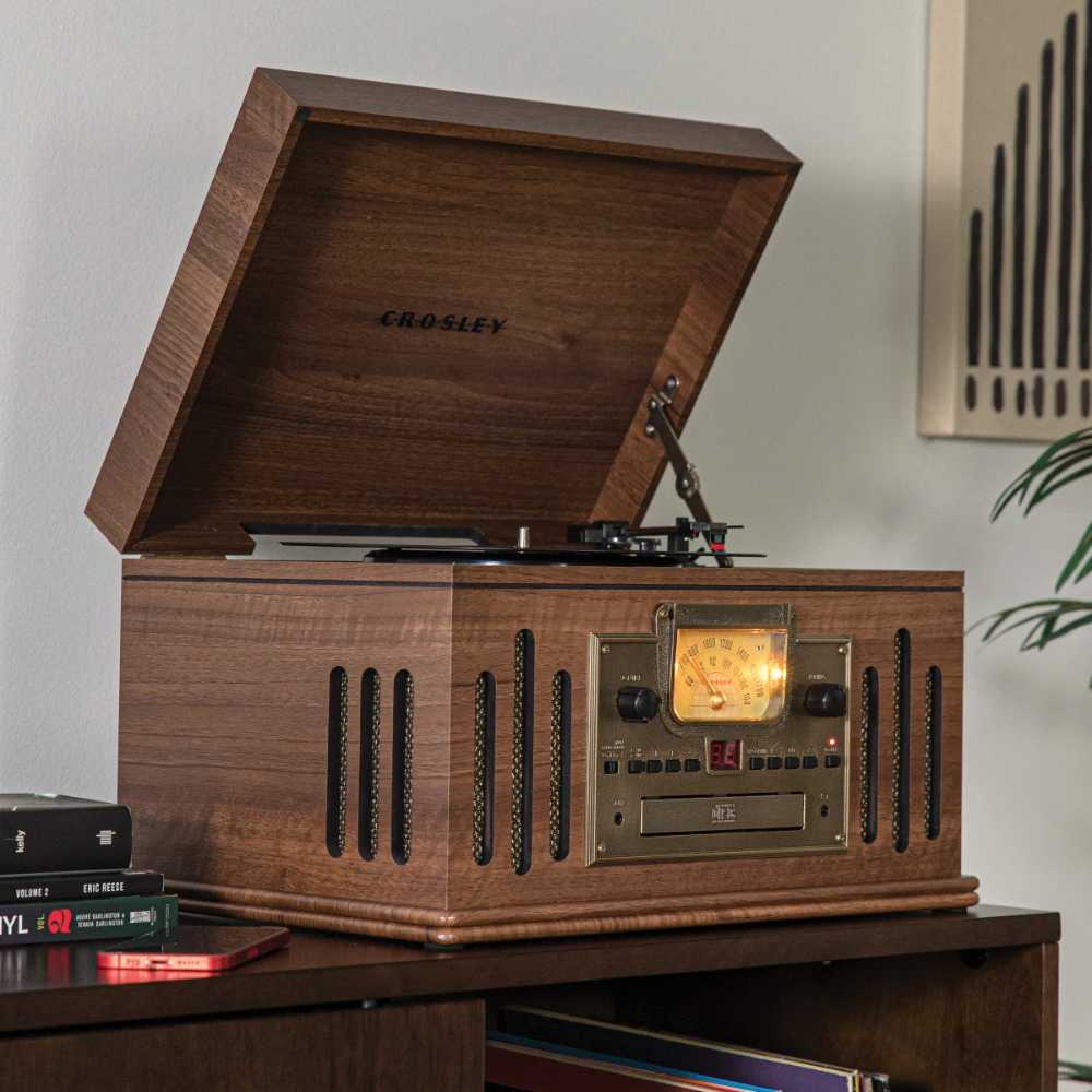 Placed on a wooden shelf, the Crosley Musician Entertainment Center - Walnut highlights its vintage radio dial, turntable, and speaker grilles