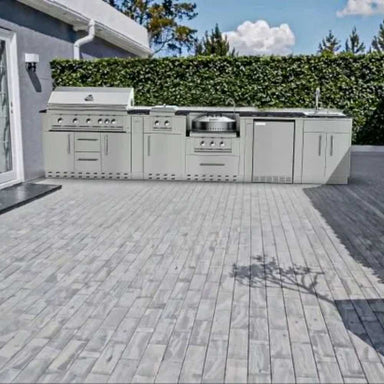 Sunstone Hill Country 13.6ft Outdoor Grill & Cabinet Island Package is installed on a sleek gray tiled patio backed by a tall privacy hedge
