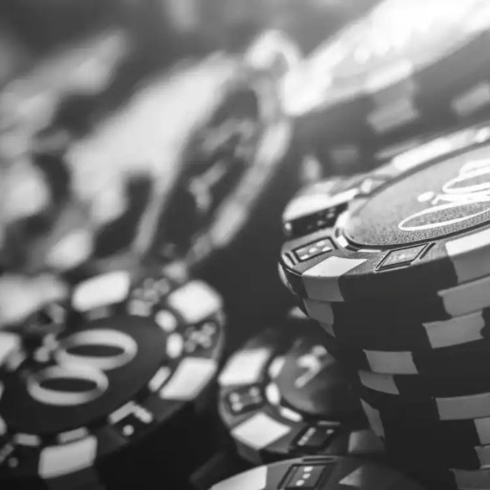 A close-up black and white image of stacked poker chips on a table, highlighting the texture and details—Reason Pros Choose Crown Casino Poker Chips for their premium weight and feel