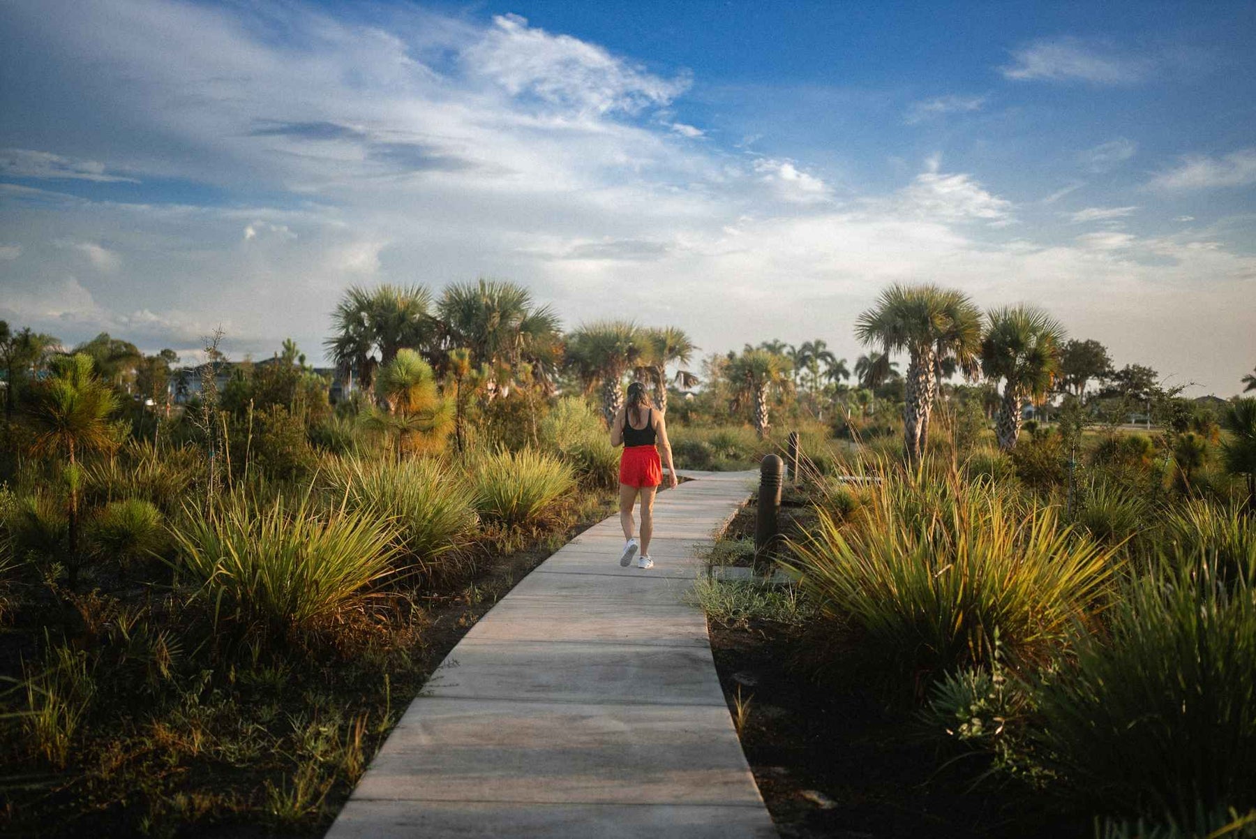 A woman walks alone on a paved path through a tropical landscape under a bright sky, representing one of the 15 Outdoor Activities for Summer to Boost Mental Health