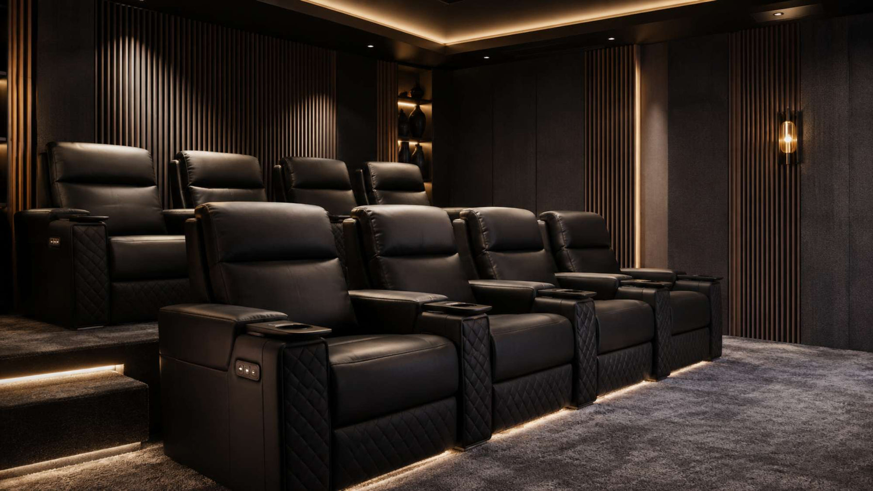 Black leather home theater seating arranged in two tiered rows inside a dark cinema room with warm accent lighting and gray carpet