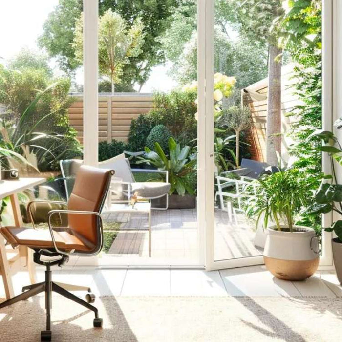 Bright home office with wooden desk, computer, plants, and open glass doors to a sunny garden, ideal for a podcast studio rental setup