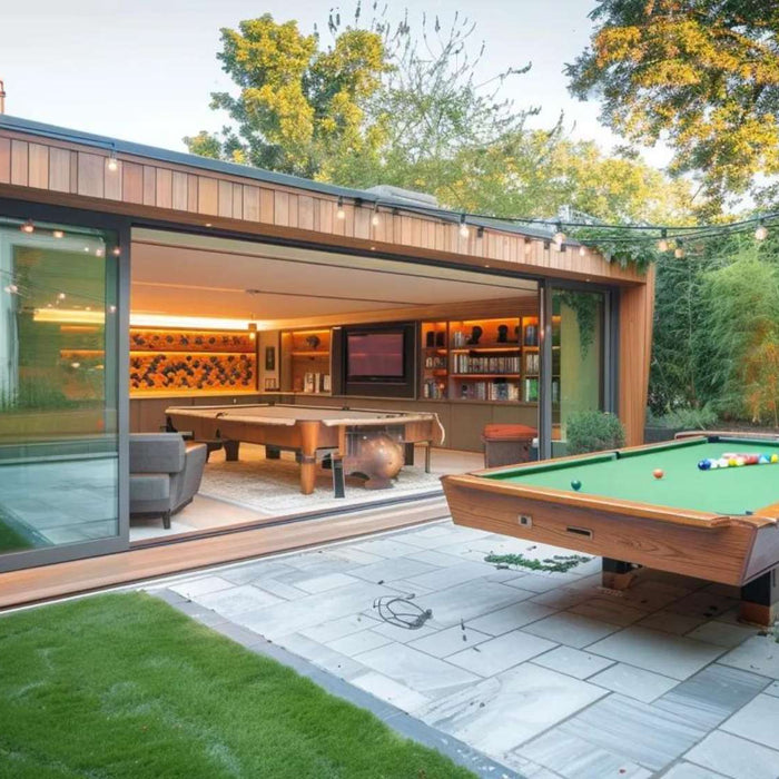 Modern backyard outdoor game room rental with a pool table on a patio, string lights overhead, and a stylish indoor lounge visible through large glass doors