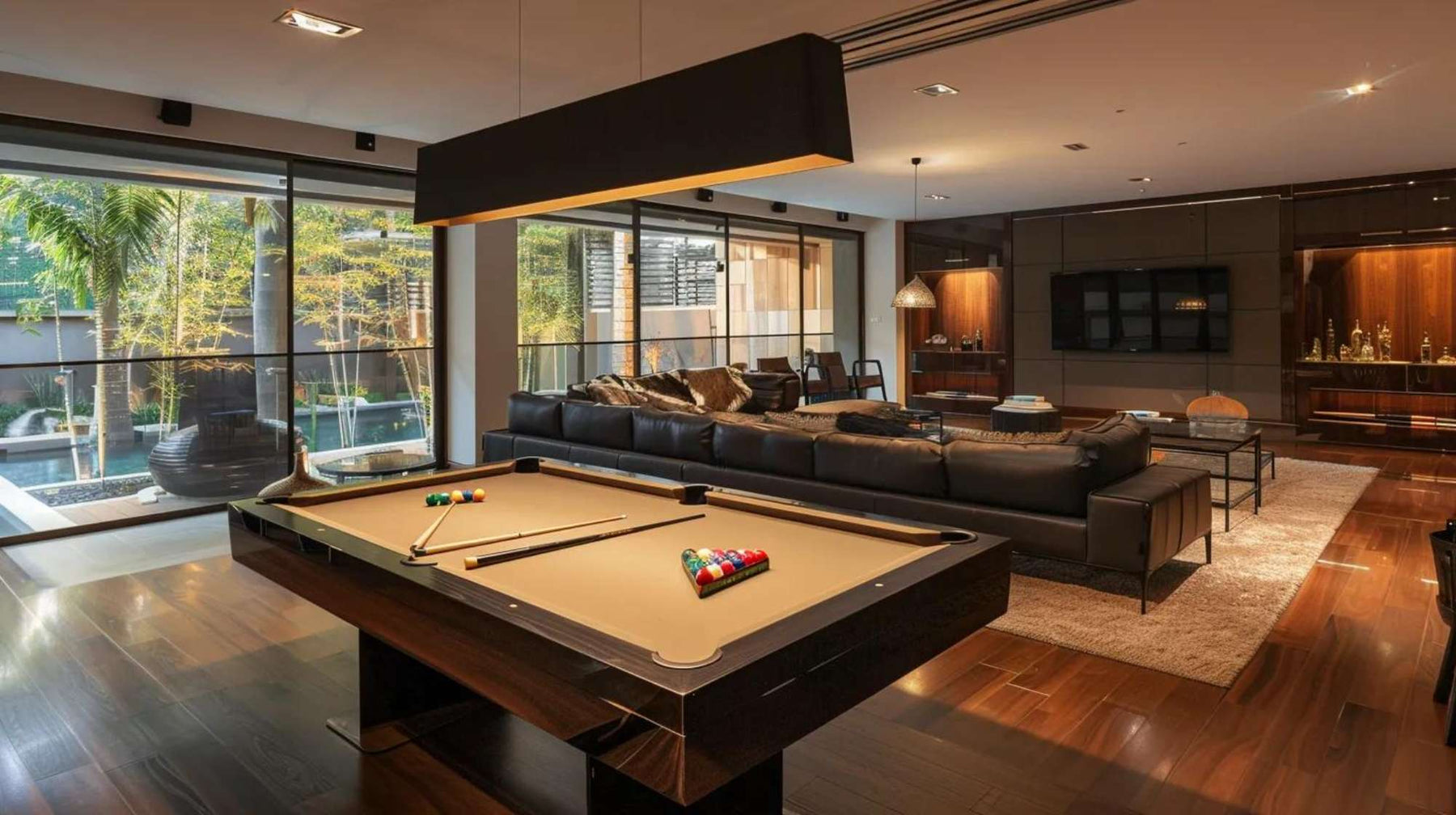 Modern man cave with pool table showing a sleek billiards table, black leather sofa, warm wood floors, and large windows letting in natural light.