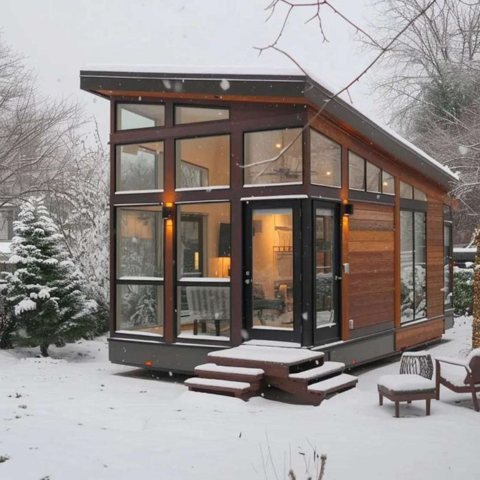 Modern tiny home with large windows sits in a snowy backyard, warmly lit inside, showing that can tiny homes survive the winter when properly designed and insulated