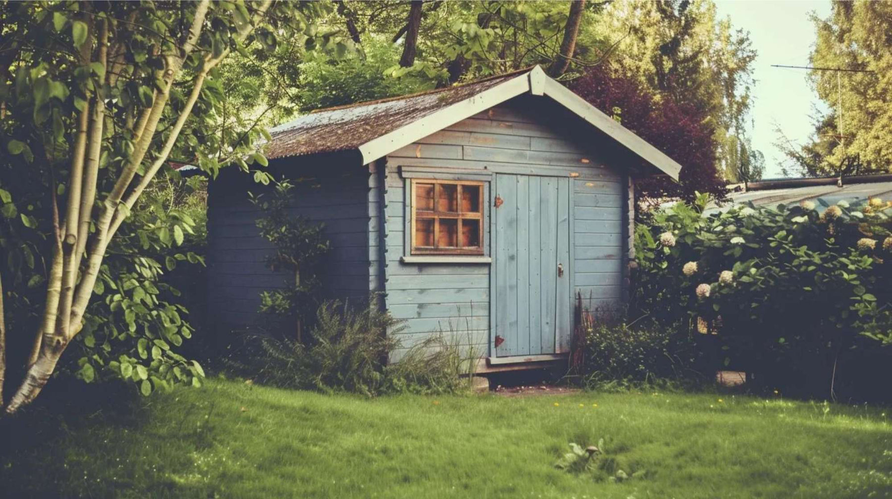Small blue wooden garden building surrounded by trees and greenery, showing a simple passive income shed placed in a quiet backyard