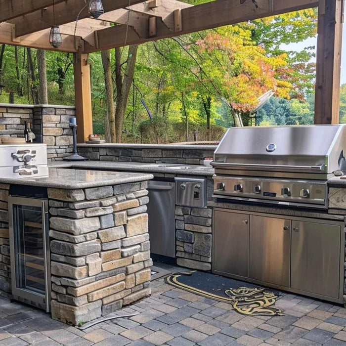 Stone outdoor kitchen with a stainless steel grill, mini fridge, counters, and wooded views creates a polished man cave BBQ setup