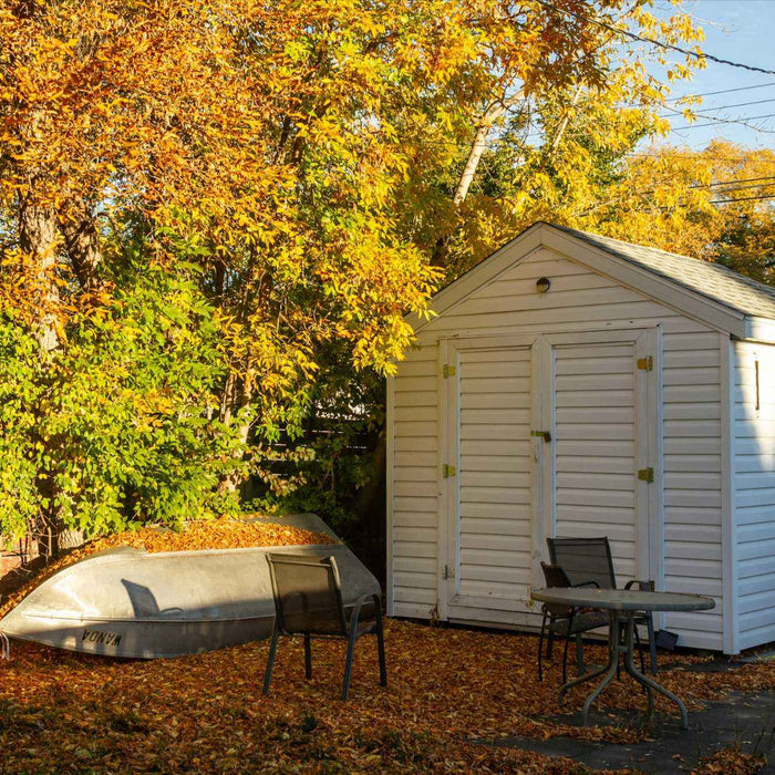 Three chairs and a round table rest on leaf-covered ground near the shed, highlighting how 7 Creative Shed Ideas can blend storage and relaxing outdoor setups