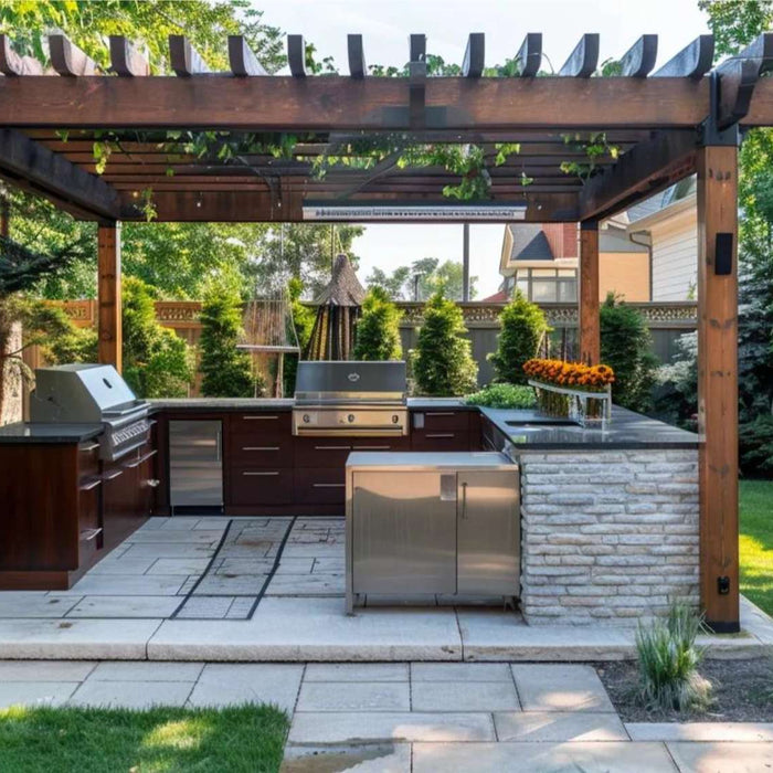 Well-organized backyard meal prep kitchen under a wooden pergola with a grill, sink, fridge, and counter space surrounded by a green garden and fenced yard