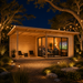 A light wood studio cabin with glass doors at night, featuring a lit interior with people watching a television.