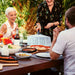 12" Ooni Perforated Pizza Peel held by a man at an outdoor dining table with friends, pizza and side dishes on the table.
