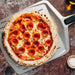 14" Ooni Perforated Pizza Peel seen from above with a cooked pepperoni pizza on the blade and the ooni logo beside it on a rusty metal surface.