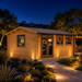 Rectangular wood cabin with glass doors and windows illuminated at night, featuring a stone path and garden landscape.
