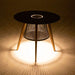 Westminster Teak Luna Small Table is illuminated from below, casting a warm glowing light through its wire base and creating a soft patterned reflection on the floor