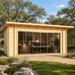 Rectangular wood studio with glass sliding doors and two people working inside a furnished office, set outdoors near trees.