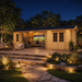 Rectangular wood cabin with glass doors and windows illuminated at night on a stone patio with outdoor seating.