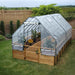 A clear plastic greenhouse cover protects the Outdoor Living Today 8×16 Raised Garden Bed, with tall green plants and flowers growing inside