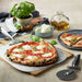 A freshly baked pizza on a peel sits beside ingredients and pizza tools made for Breville® Smart Oven® Pizzaiolo Pizza Oven