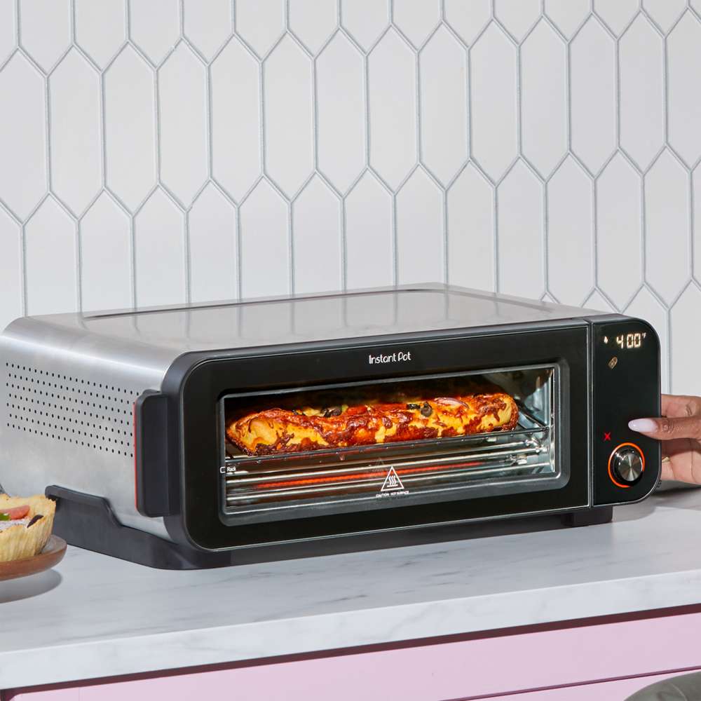 A pizza cooks inside Instant Pot® InstantHeat™ Pizza Oven while a hand adjusts the control dial to 400°F