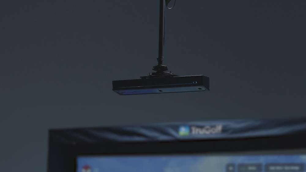 A slim ceiling-mounted sensor with blue lighting is part of TruGolf APOGEE Golf Launch Monitor w/ Starter 10 (2025) Enclosure + Gimme Package