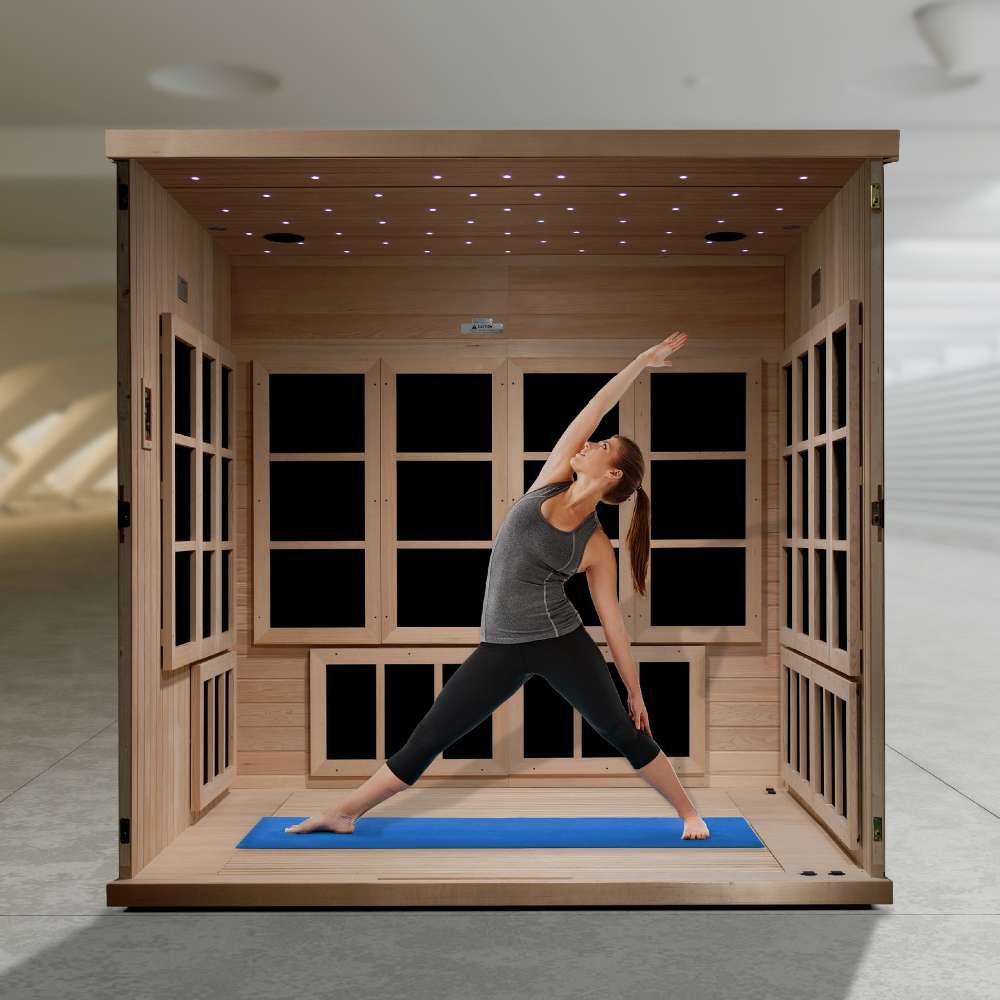 A woman holds a yoga pose on a blue mat inside Golden Designs Catalonia 8 Person Near Zero EMF Far IR Sauna with its benches removed