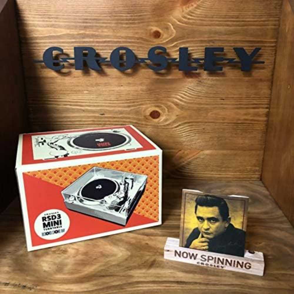 A Crosley RSD3 Mini Turntable for 3 Inch Vinyl Records w Johnny Cash Single is displayed with its box and a vinyl stand featuring Johnny Cash's portrait