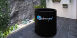 A Dreampod Cold Plunge Barrel FLEX with Chiller is displayed in a peaceful, plant-filled outdoor area with a rock wall backdrop