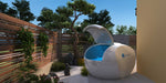 A Dreampod Home Float Plus with its lid open is situated on a patio in a tranquil garden setting with plants and decorative stones