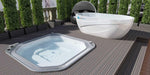 A Dreampod Ice Bath with Chiller is placed on a spacious deck next to a hexagonal hot tub, surrounded by lush green hedges