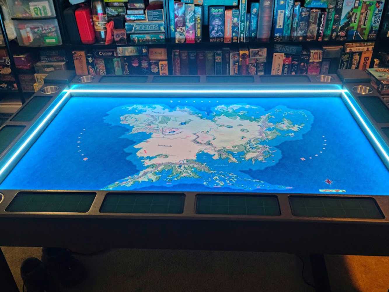 A Game Theory Tables Origins Lit table with a brightly lit map of a fantasy world in the center, surrounded by a collection of board games on shelves in the background