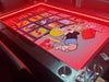 A Game Theory Tables Origins Lit table with a vibrant, comic-inspired Richie Rich design under red lighting