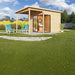 A stylish wooden cabin with a slanted roof and large glass doors stands in a lush garden with mountain views, showcasing the GardenHouse24 USA ALU Concept 70F Garden Room
