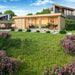A stylish GardenHouse24 USA ALU Concept 70L Garden Room sits in a landscaped yard, with floor-to-ceiling windows revealing a cozy interior with green sofas and a dining set