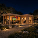 L-shaped wood cabin with glass walls at night, showing people watching a screen inside the ALU Concept Quinta 70. large glass doors and a shaded porch