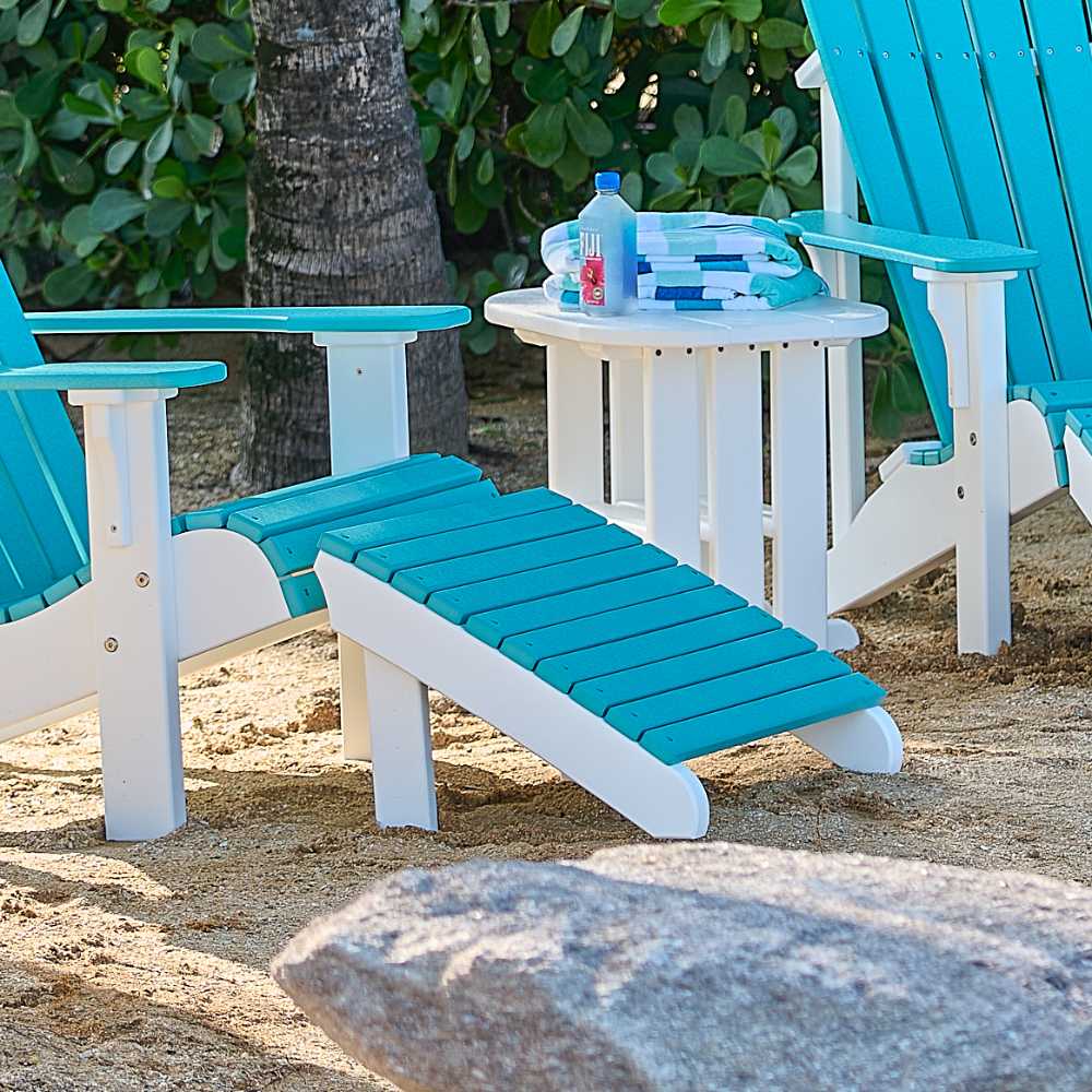 A LuxCraft Deluxe Adirondack Footrest in turquoise is set outdoors beside a matching Adirondack chair and a white table