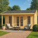 A GardenHouse24 USA Lilja 70 Garden Room large glass double doors and windows, featuring two cushioned armchairs and a coffee table on a brick patio