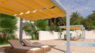 A Structureworks Balance Trex Pergola with a bright yellow canopy provides shaded lounging space beside a modern pool with palm trees