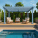 A Structureworks Reverie Fiberglass Pergola in a light blue color shades three cushioned chairs on a wooden poolside deck